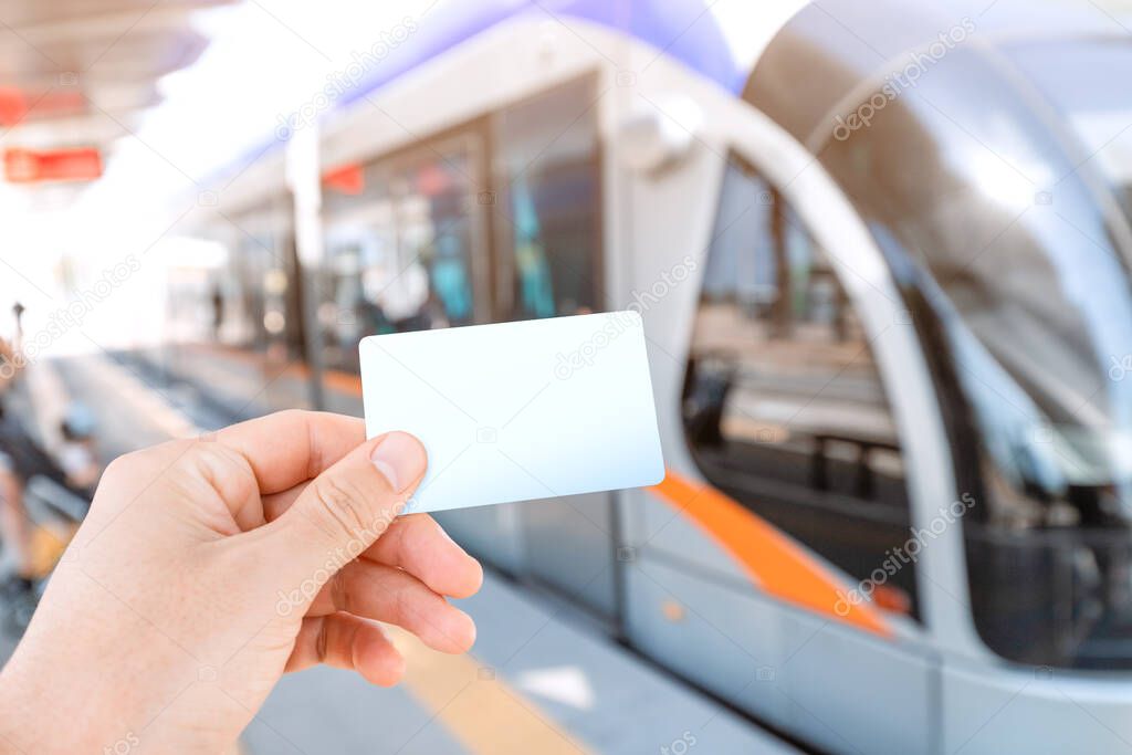 Hand of a passenger holding white empty card for contactless and cashless paying for modern urban transport system in the city