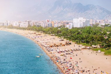 Crowded Antalya city Konyaalti beach with hundreds of vacationers and tourists resting, sunbathing and swimming at extremely hot summer day in resort town