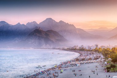 Sunset HDR effect view of scenic and popular Konyaalti beach in Antalya resort town. Majestic mountains with haze in the background. Vacation and holiday in Turkiye