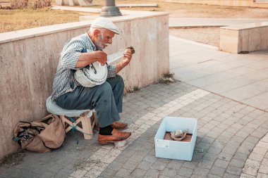 21 June 2022, Antalya, Turkey: Senior man playing on folk traditional musical instrument - saz and begging for money at city street
