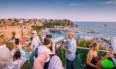 21 June 2022, Antalya, Turkey: Crowds of people tourists at the observation viewpoint using binoculars and looking to old town harbor with yachts and cruise ships