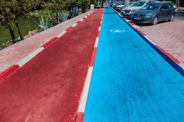 23 June 2022, Antalya, Turkey: Painted blue Bicycle lane and red walking path in city park. Eco environment and green and healthy transport. Bike path