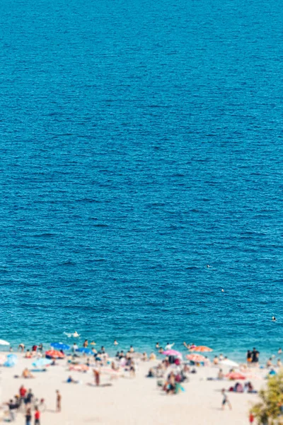 Sunny beach with lounge chairs and sunbeds and vacationers swimming and chilling in refreshing sea waters