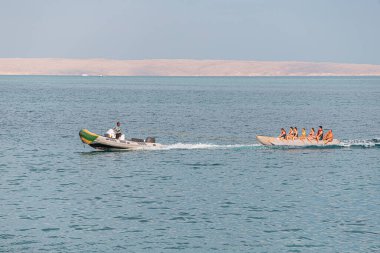 09 January 2022, Hurghada, Egypt: Tourists and vacationers have fun on an inflatable banana tied to a speed boat. Sea activities and recreation