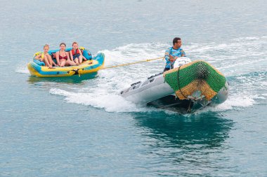 09 January 2022, Hurghada, Egypt: Tourists and vacationers have fun on an inflatable banana tied to a speed boat. Sea activities and recreation