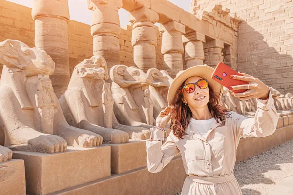 Travel blogger woman takes selfie photos among Pharaoh statues at the ruins of the famous Karnak temple in Luxor in Egypt