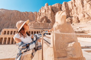 Happy woman traveler explores the ruins of the ancient Egyptian Hatshepsut temple in the heritage city of Luxor. Wonders of the World and tourist experience