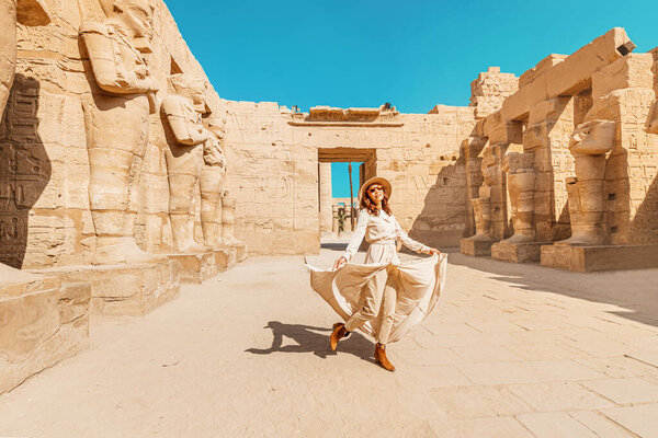 A happy tourist girl in a dress is interested in Egyptology and archaeology and gets a travel experience at the Karnak Temple in Luxor.