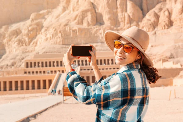 Travel blogger girl takes pictures on a smartphone at the famous Hatshepsut temple in the ancient city of Luxor in Egypt.