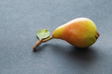 The fruit of a sweet and ripe pear with a stalk and a green leaf on a black textured background. Fresh and healthy organic bio product