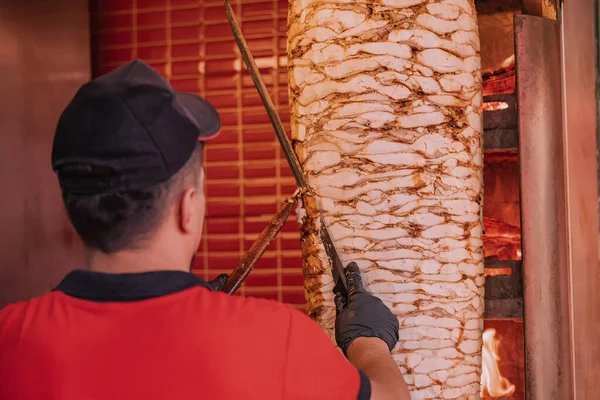 The chef prepares a doner kebab by cutting toasted slices of meat from the grill spit in a fast food restaurant.