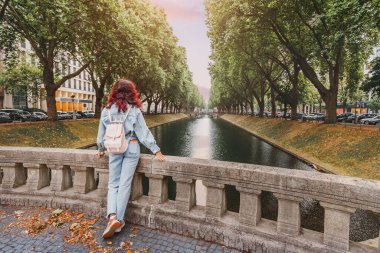 Düsseldorf, Almanya 'da zengin tarihi olan Konigsallee su kanalı yakınında duran sırt çantalı mutlu turist kadın.