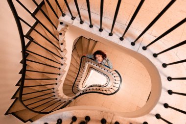 Geometrik spiral desen evdeki merdivenlerin mimari unsurlarını genişletiyor ve kıza poz veriyor.