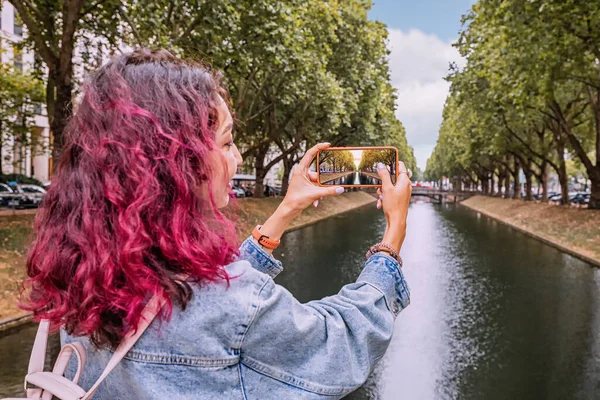 Happy girl travel blogger takes photos on her smartphone of the famous Konigsallee canal in the old town of Dusseldorf, Germany. Travel and sightseeing locations