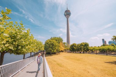 Düsseldorf TV kulesine bakan Ren nehri üzerindeki yaya yolu köprüsünden geçen bir kız gezgin. Almanya 'nın turistik bölgeleri ve eğlence merkezleri