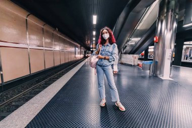 Korunaklı tıbbi maskeli bir kız koronavirüs salgını sırasında metroda trenini bekliyor.