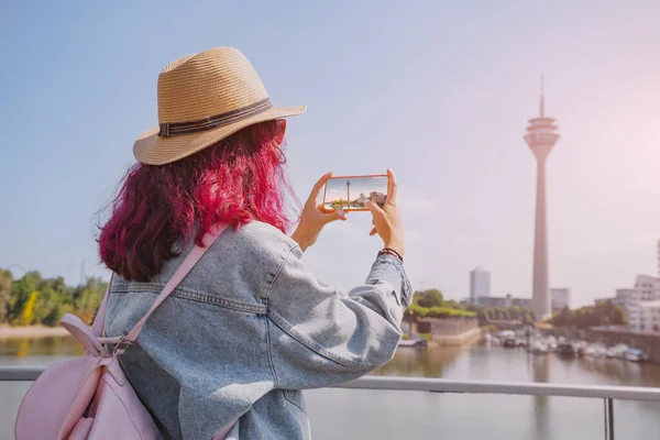 Happy girl travel blogger takes pictures on her smartphone of the famous Dusseldorf TV tower from the Media Harbor canal in the post industrial district. Travel and sightseeing locations