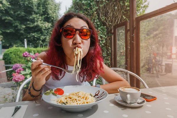 The girl is in a funny hurry and eats Italian pasta in a cafe. The concept of good manners and rules of etiquette on the first date