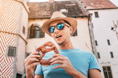 Eski bir Alman binasının arka planında lezzetli kraker yiyen mutlu bir erkek turist. Seyahat ve turizm mutfağı