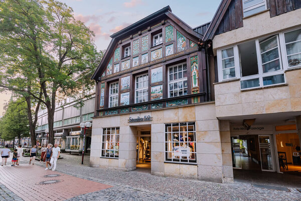 24 July 2022, Osnabruck, Germany: People and tourists walking by old town street with picterisque half-timbered and fachwerk architecture buildings, accommodating hotels and shops