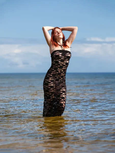 Femme en robe noire contre la mer — Photo