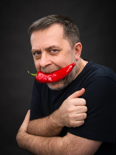 Äldre man med röd paprika i munnen — Stockfoto