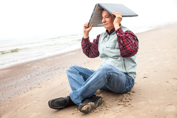 Oude man met laptop op strand — Stockfoto