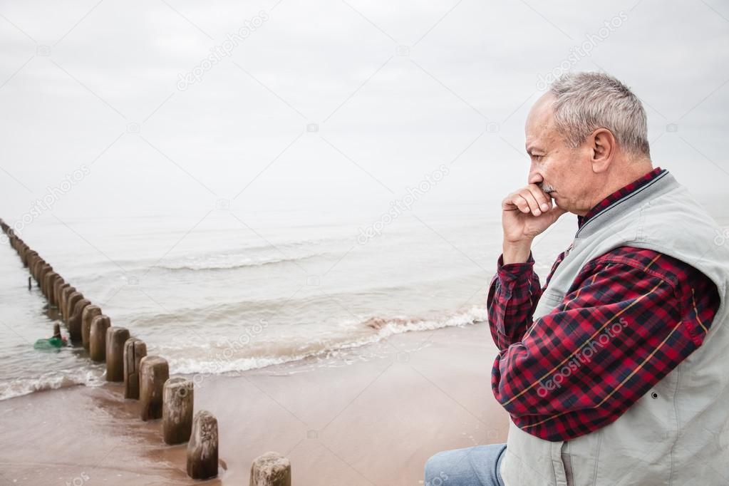 Thoughtful elderly man standing on the beach