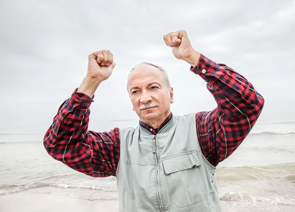 Older man with hands up at the coast — Stock Photo, Image