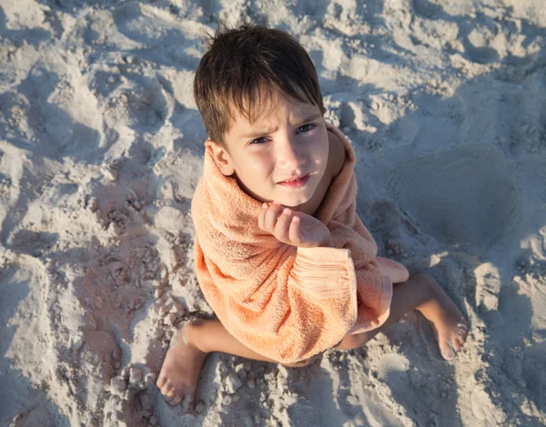 Menino embrulhado em toalha sentado na praia de areia — Fotografia de Stock