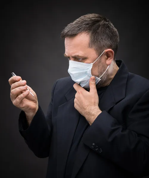 Homme en masque médical avec un thermomètre — Photo