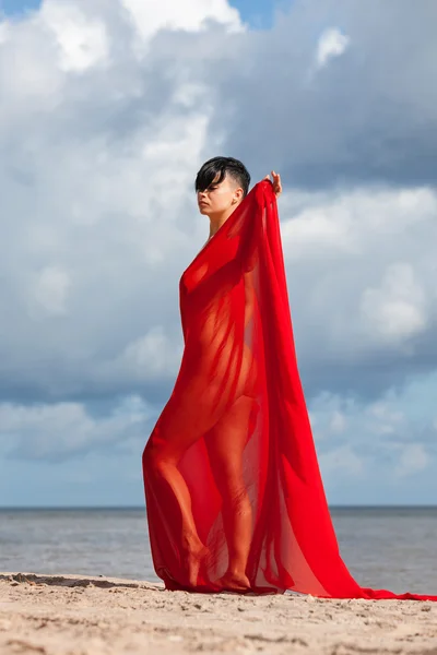 Mulher nua em uma praia com tecido vermelho — Fotografia de Stock