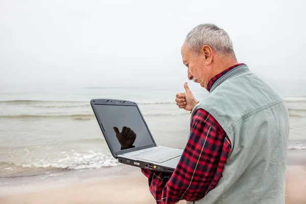 Vecchio in piedi sulla spiaggia con un computer portatile — Foto Stock