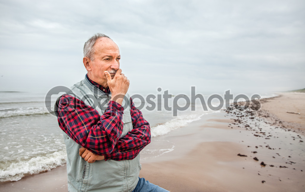 Thoughtful elderly man standing on the beach