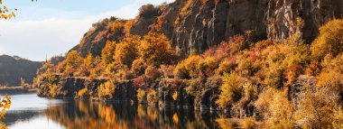 Sel basmış eski taş ocağında renkli ağaçlarla dolu altın bir sonbahar. Kayalar, göl ve sarı ağaçlar