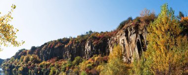 Sel basmış eski taş ocağında renkli ağaçlarla dolu altın bir sonbahar. Kayalar, göl ve sarı ağaçlar