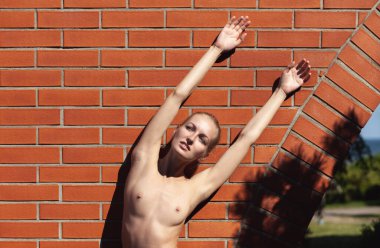 Açık havada çıplak bir kadın. Tuğla duvarın yanında poz veren genç ve güzel bir kadın.