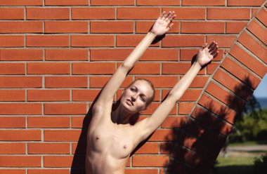 Açık havada çıplak bir kadın. Tuğla duvarın yanında poz veren genç ve güzel bir kadın.