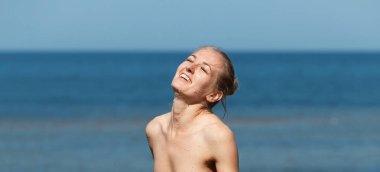 Güzel, çıplak, genç bir kadın sahilde havuz kenarında duş alıyor.