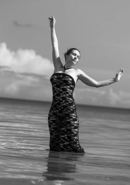 Siyah dantel elbiseli genç, kızıl saçlı kadın sahilde çıplak poz veriyor.