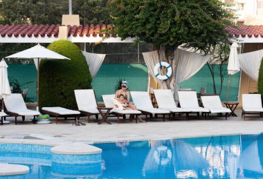 Mutlu aile ve sağlıklı yaşam tarzı. Havuz kenarında küçük çocuğu olan genç anne dinleniyor.