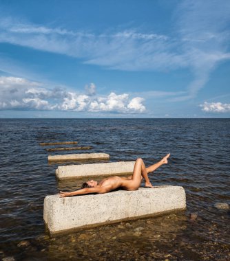Bu yalanı denizde bir güneşli yaz gün Beton üzerinde güneşlenme üzerinde genç çıplak kadın tabaka