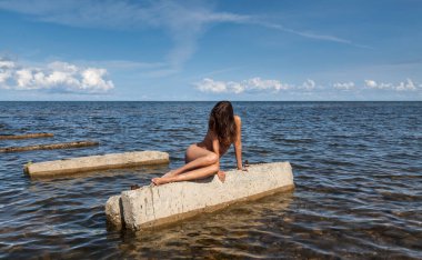 Bu yalanı denizde bir güneşli yaz gün Beton üzerinde güneşlenme üzerinde genç çıplak kadın tabaka