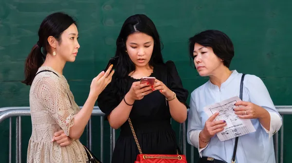 2017年9月17日 緑の壁に立ち ニューヨークのマンハッタンの路上でスマートフォンや広告ブックレットを使って情報を探すアジア系女性3人 — ストック写真