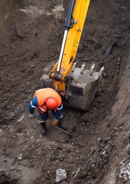 KYIV, UKRAINE - 20 Mayıs 2021: Şehrin şantiyesindeki toprak çalışmaları. Şehrin kanalizasyon sisteminde tamirat. Kürekli özel takım elbiseli bir işçi.