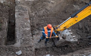 KYIV, UKRAINE - 20 Mayıs 2021: Şehrin şantiyesindeki toprak çalışmaları. Şehrin kanalizasyon sisteminde tamirat. Kürekli özel takım elbiseli bir işçi.