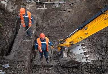 KYIV, UKRAINE - 20 Mayıs 2021: Şehrin şantiyesindeki toprak çalışmaları. Şehrin kanalizasyon sisteminde tamirat. Kürekli özel takım elbiseli bir işçi.