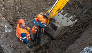 KYIV, UKRAINE - 20 Mayıs 2021: Şehrin şantiyesindeki toprak çalışmaları. Şehrin kanalizasyon sisteminde tamirat. Kürekli özel takım elbiseli bir işçi.