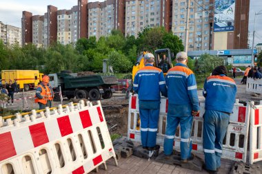 KYIV, UKRAINE - 20 Mayıs 2021: Şehrin şantiyesindeki toprak çalışmaları. Şehrin kanalizasyon sisteminde tamirat. Kürekli özel takım elbiseli bir işçi.