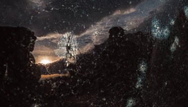 Arabanın kırık camında gün batımının yansıması. Araba camı bir taşla parçalanmış. Kırık araba ön camı. Kriminal olaylar. Vandallar, holiganlar arabayı parçaladı, ön camı kırdı.